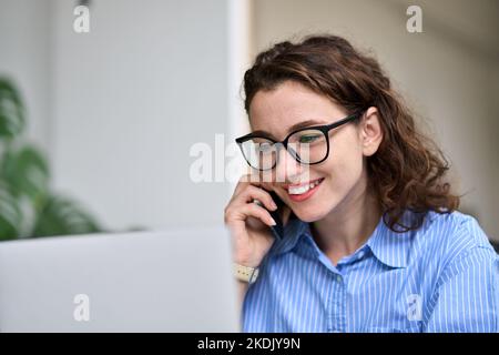 Young woman talking on the phone using laptop working online. Stock Photo