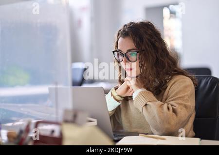 Young professional woman using laptop watching online webinar at work. Stock Photo