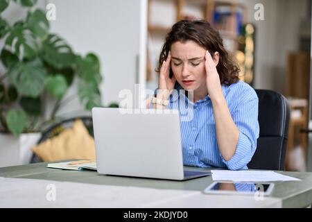 Stressed young woman employee touching head feeling headache fatigue at work. Stock Photo