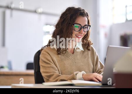 Young happy woman employee or student sitting at desk using laptop. Stock Photo