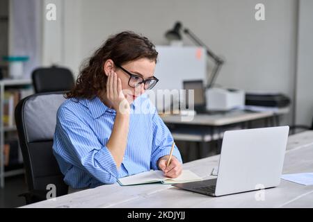 Young business woman using laptop watching online webinar at work in office. Stock Photo