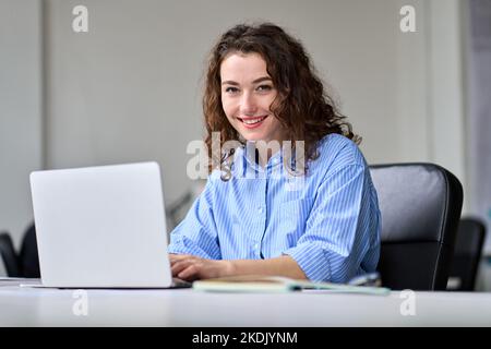 Young happy business woman sitting at office desk working on laptop. Portrait Stock Photo