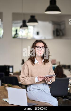 Young happy business woman holding tablet posing in office, vertical. Stock Photo