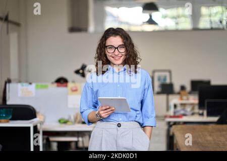 Young happy business woman holding tablet standing in office, portrait. Stock Photo