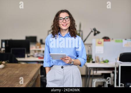 Young happy female manager holding tablet standing in office, portrait. Stock Photo