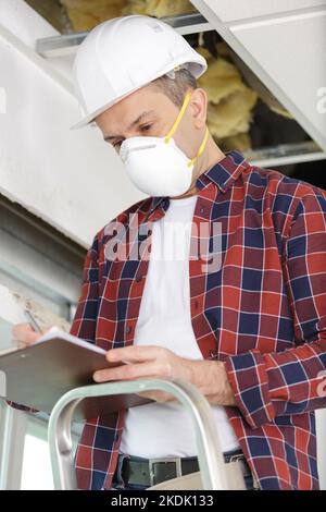 worker with mask holding black clipboard and thinking Stock Photo