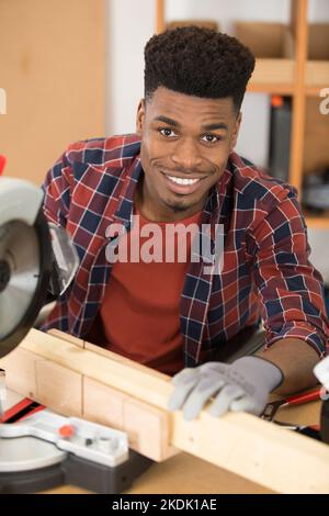 happy workman cutting wooden planks using circular saw in workshop Stock Photo