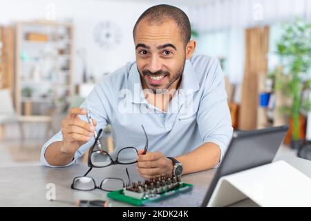 man follows online instructions on tablet to repairs eyeglasses Stock Photo