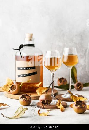 Two glasses with homemade wine or liquor of medlar ripe fruits. Alcohol drink concept. Selective focus. Copy space. (Mespilus germanica) Stock Photo