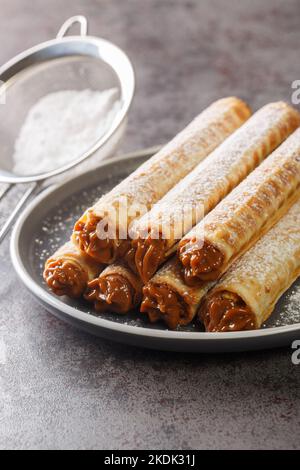 Concept of breakfast with wafer rolls with condensed milk closeup in plate on the table. Vertical Stock Photo