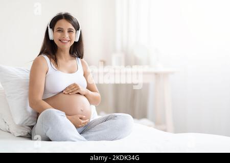 Happy smiling young pregnant woman listening to music, using headphones Stock Photo