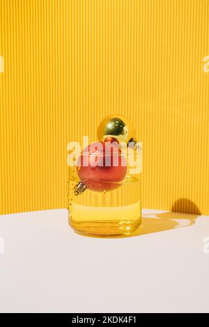 Two Christmas baubles in drinking glass with ribbed yellow paper background. Minimal holiday greeting concept. Stock Photo