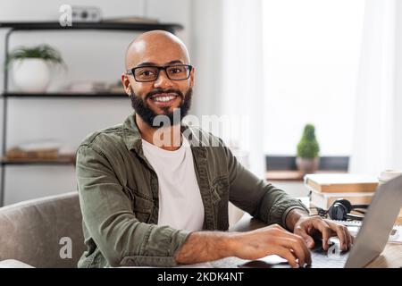Portrait of happy mature latin man sitting at desk, working on pc laptop and smiling at camera, free space Stock Photo