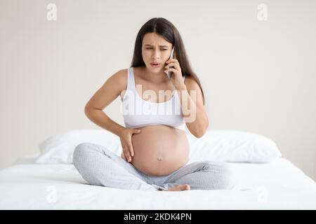 Pregnant woman in pain calling doctor, home interior Stock Photo