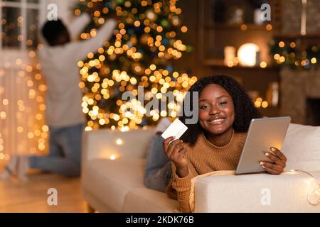 Young Man Using Tablet A young African American woman decorates a red holiday gift in a cozy ...