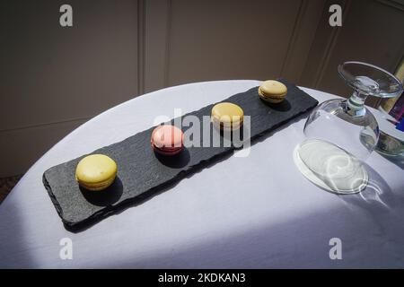 Macaroons on a slate board with a water glass on a table with a white tablecloth. Stock Photo