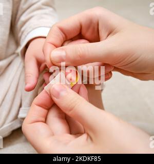 Woman mother sticks a medical band-aid on the toddler baby finger. Mom s hand with a sticky wound protection bandage and a child hand. Kid aged one ye Stock Photo