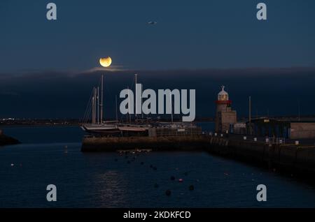 The November 2021 partial lunar eclipse setting at Howth Harbour. Stock Photo