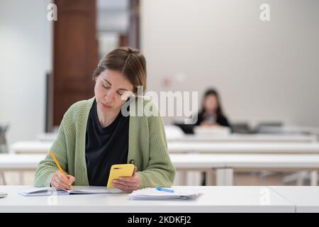 Concentrated mature female student using smartphone for exam preparation, taking second degree Stock Photo