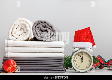 Stack of folded rolls of towels and bed sheets, sheet on table with christmas decor and alarm clock Stock Photo