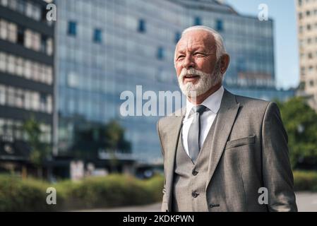 Contemplating male professional looking away. Senior entrepreneur is standing against buildings. He is wearing suit during business travel in the city Stock Photo