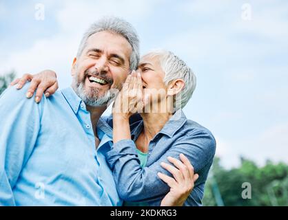 senior couple happy elderly love together retirement lifestyle smiling man woman mature ear gossip secret whispering whisper Stock Photo