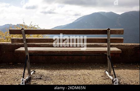 Empty wooden bench, mountain view, cloudy sky background. Back view of lonely bench in countryside, Autumn Stock Photo