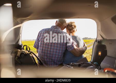 Happy senior couple sitting in car open trunk in the wild Stock Photo