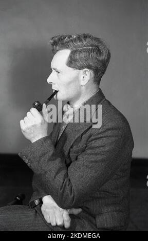 1960s, historical, a side view of a man wearing a herring bone tweed suit and rolled-neck sweater, smoking his pipe, deep in thought, England, UK. Stock Photo