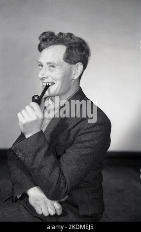 1960s, historical, sitting for his photo, smiling, a man wearing a herring bone tweed suit and rolled-neck sweater, smoking his pipe, England, UK. Stock Photo