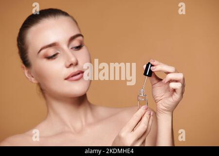 beautiful woman holding bottle with serum for skin care on beige background Stock Photo