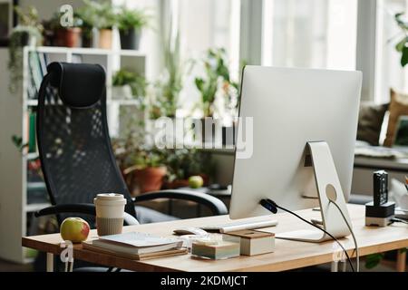 Workplace of modern white collar worker with computer monitor, fresh apple and cup of coffee and black armchair in coworking space Stock Photo