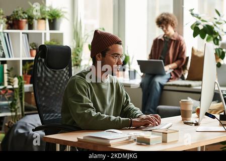 Young serious webdesigner in casualwear working over new website on computer while sitting in front of monitor and typing Stock Photo