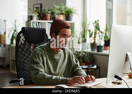 Young serious IT engineer working with coded information while sitting by desk in front of computer monitor in openspace office Stock Photo