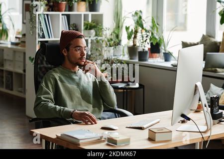 Young serious businessman looking at computer screen while watching online video or waiting for website page uploading Stock Photo