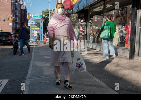 A Muslim woman out shopping and wearing pink clothing walks on 74th street in Jackson Heights, Queens, New York City. Stock Photo
