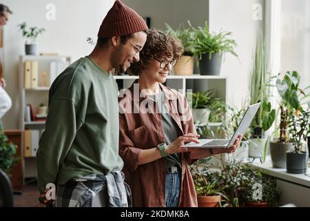 Two young software developers discussing online information and their ideas while creating new program with help of online advice Stock Photo