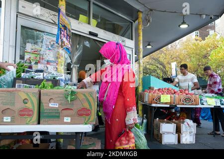 A woman wearing a hijab and face mask shops for Pohi Saag vegetables at the Apna Supermarket on 37th Avenue in Jackson Heights, Queens, New York City. Stock Photo