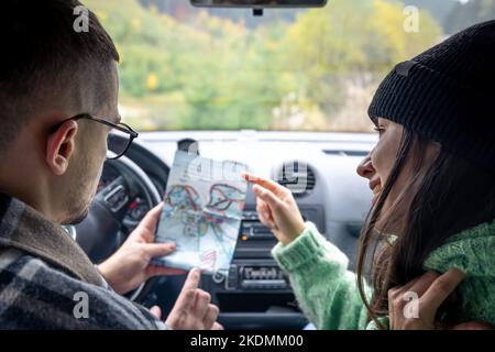 A man and lady holding and looking at paper map, sitting inside car. Stock Photo