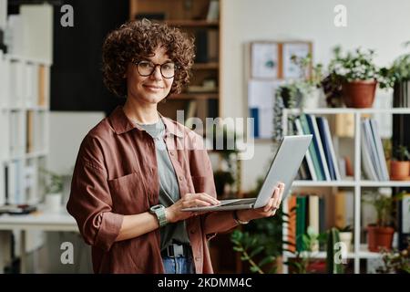 Young successful manager in casualwear standing in front of camera in coworking space and using laptop while analyzing online data Stock Photo