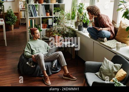 Two young designers or IT engineers with mobile gadgets having discussion of working points or organizing work at meeting Stock Photo