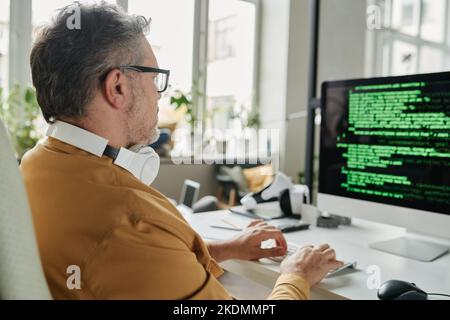 Selective focus on mature IT engineer decoding information on computer screen while sitting in front of monitor in coworking space Stock Photo