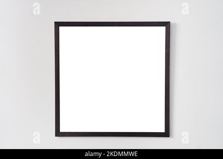 An empty square photo frame with a black border hanging on a white wall Stock Photo