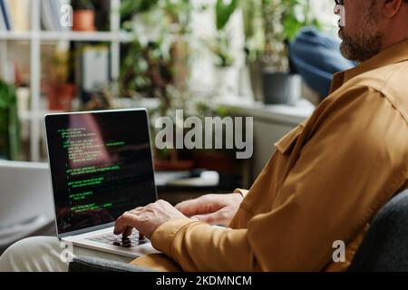 Selective focus on mature IT support engineer decoding data on laptop screen while sitting in openspace office with green house plants Stock Photo