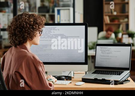 Young IT engineer looking at laptop screen with coded data and decoding it while developing new software in coworking space Stock Photo