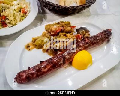 Grilled Greek sausage and vegetables placed on a dining table in Greece local restaurant. Stock Photo