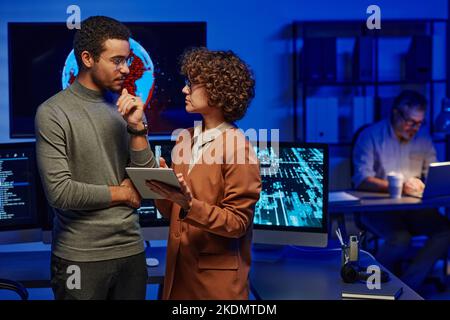 Two young confident programmers discussing ideas for new creative project while woman with tablet making presentation of some points Stock Photo
