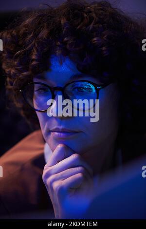 Young busineswoman with pensive facial expression sitting in front of computer and looking at screen while concentrating on work Stock Photo