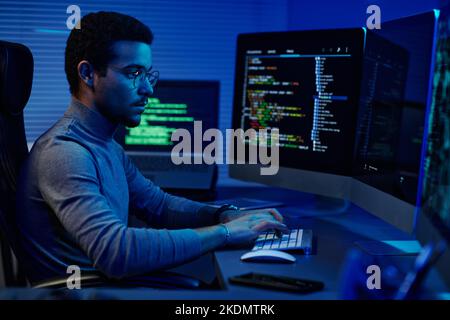Young serious software developer typing on desktop keyboard while working in front of computer monitors in server room Stock Photo