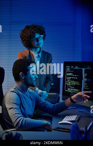 Confident IT engineer or software developer pointing at codes on computer screen while making presentation to female colleague Stock Photo